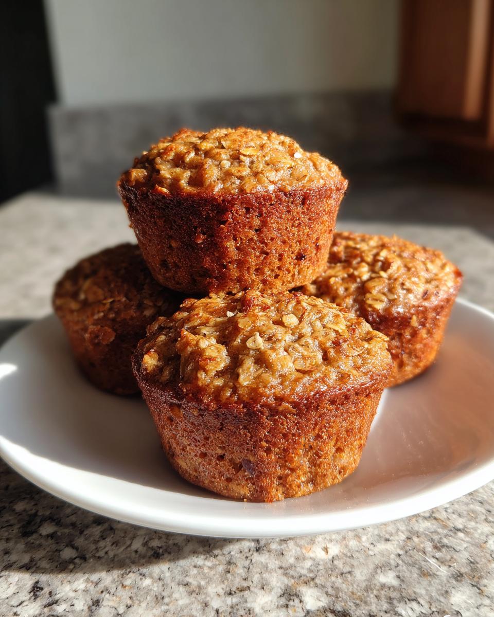Four golden brown banana oatmeal muffins stacked on a white plate, catching bright sunlight.