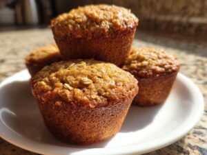 A stack of four moist banana oatmeal muffins with visible oats on top, sitting on a white plate.