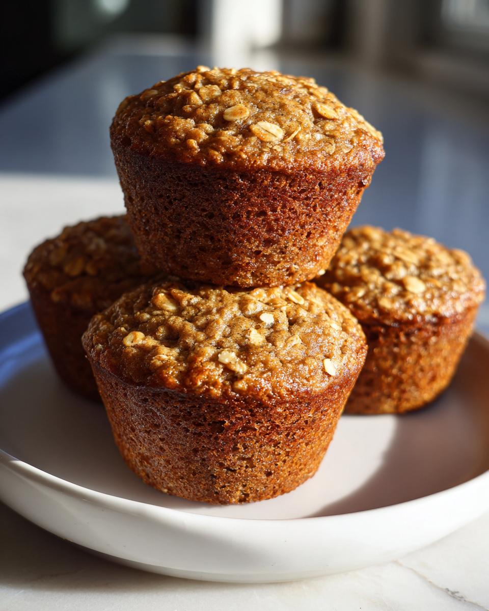 A stack of four moist banana oatmeal muffins with visible oat topping, sitting on a white plate.