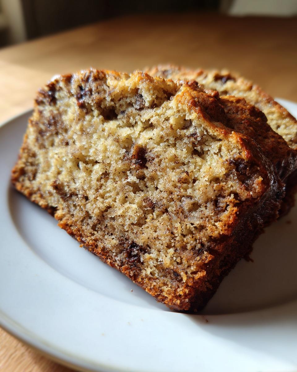 Close-up of two moist slices of protein banana bread with visible chocolate chips on a white plate.