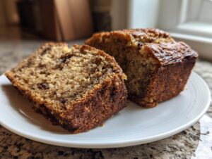 Two thick slices of moist protein banana bread with a dark, caramelized crust served on a white plate.