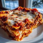 A thick, layered slice of ravioli lasagna with rich meat sauce and bubbly melted cheese topping.