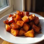 A close-up of caramelized, perfectly roasted sweet potatoes cubes piled on a white plate.