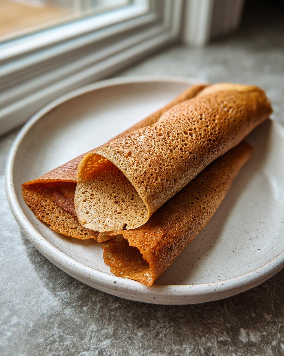 Two rolled, golden-brown cottage cheese wraps resting on a light, speckled ceramic plate near a window.