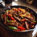 Close-up of sizzling steak fajita strips mixed with colorful bell peppers and onions in a black cast iron skillet.
