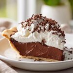 A perfect slice of chocolate cream pie featuring a thick chocolate layer, topped with whipped cream and chocolate shavings.
