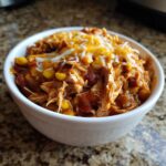 A white bowl filled with shredded slow cooker buffalo chicken chili topped with melted shredded cheddar and Monterey Jack cheese.