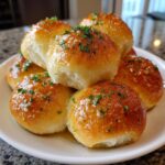 A close-up of several soft, golden brown buttery rolls brushed with garlic butter and sprinkled with parsley.