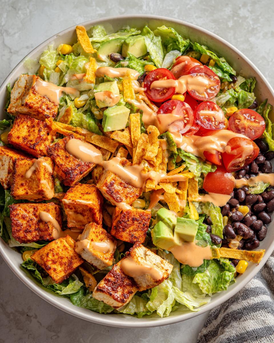 Overhead view of a vibrant Southwest salad bowl topped with seasoned tofu, avocado, black beans, and creamy dressing.