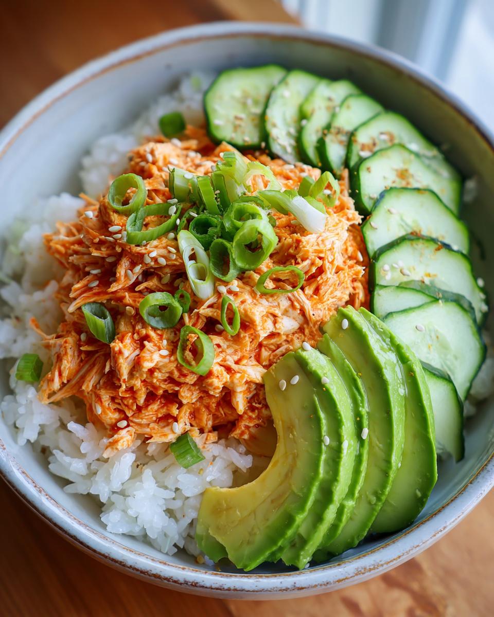 A vibrant spicy crab sushi bowl featuring shredded spicy crab mix over white rice, topped with green onions, sliced avocado, and cucumber.