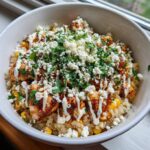 A close-up of a street corn chicken rice bowl topped with cotija cheese, cilantro, and crema.