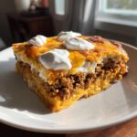 A hearty slice of taco pie featuring layers of seasoned ground beef, cheese, and topped with dollops of sour cream.