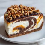 A decadent slice of turtle cheesecake featuring a marbled chocolate swirl, caramel, and topped with chocolate glaze and chopped pecans.