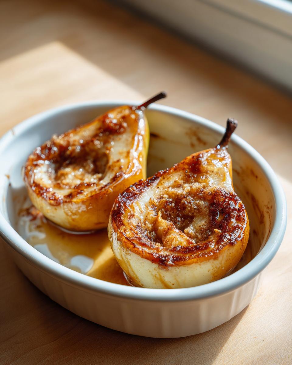 Two halves of golden baked pears, topped with caramelized cinnamon sugar, sitting in a white dish.