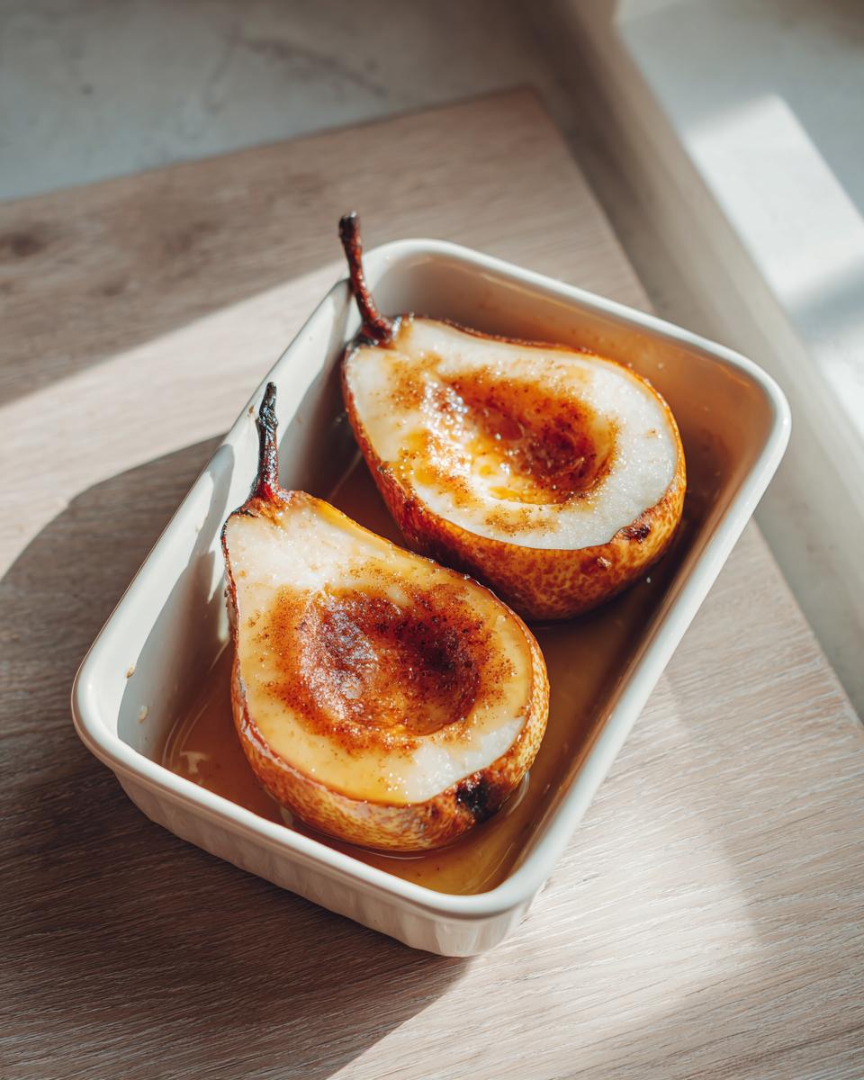 Two halves of warm baked pears, caramelized with spices, sitting in a white baking dish.