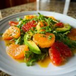 Close-up of a vibrant citrus salad featuring orange and grapefruit segments, avocado slices, and arugula.