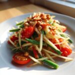 Close-up of a fresh papaya salad featuring shredded green papaya, green beans, cherry tomatoes, and crushed peanuts.