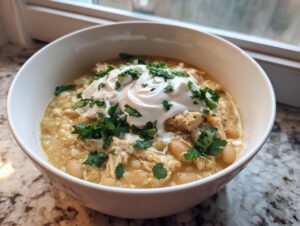 A bowl of creamy white chicken chili recipe topped with a dollop of sour cream and fresh cilantro.