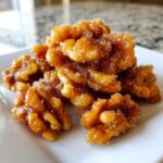 A close-up, appetizing pile of homemade candied walnuts coated in a thick, glistening sugar glaze and sprinkled with coarse sugar crystals.