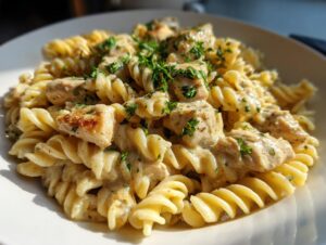 Close-up of fusilli pasta mixed with chicken pieces in a rich garlic parmesan cream sauce, garnished with parsley.