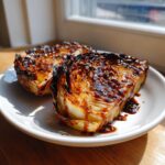 Two thick slices of perfectly roasted cabbage steaks, heavily glazed with a dark sauce and sesame seeds.