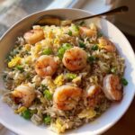 Close-up of a white bowl filled with delicious shrimp fried rice, topped with plump shrimp and green onions.