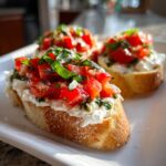 Three slices of toasted bread topped with creamy Boursin bruschetta dip, fresh diced tomatoes, and basil.
