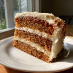 A tall slice of brown butter spice cake with three layers of cake and two layers of thick, white whipped icing.