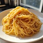 A close-up of perfectly coated buttered spaghetti, glistening under natural light on a white plate.