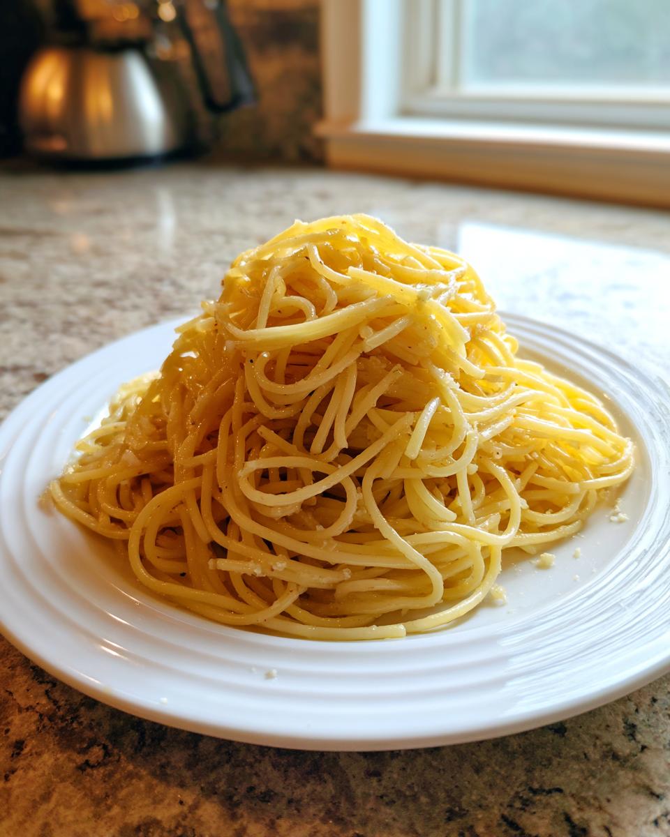 A generous serving of glistening buttered spaghetti piled high on a white plate, ready to eat.