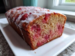 A loaf of Cinnamon Rhubarb Bread with Brown Butter, drizzled with white icing, resting on a white platter.