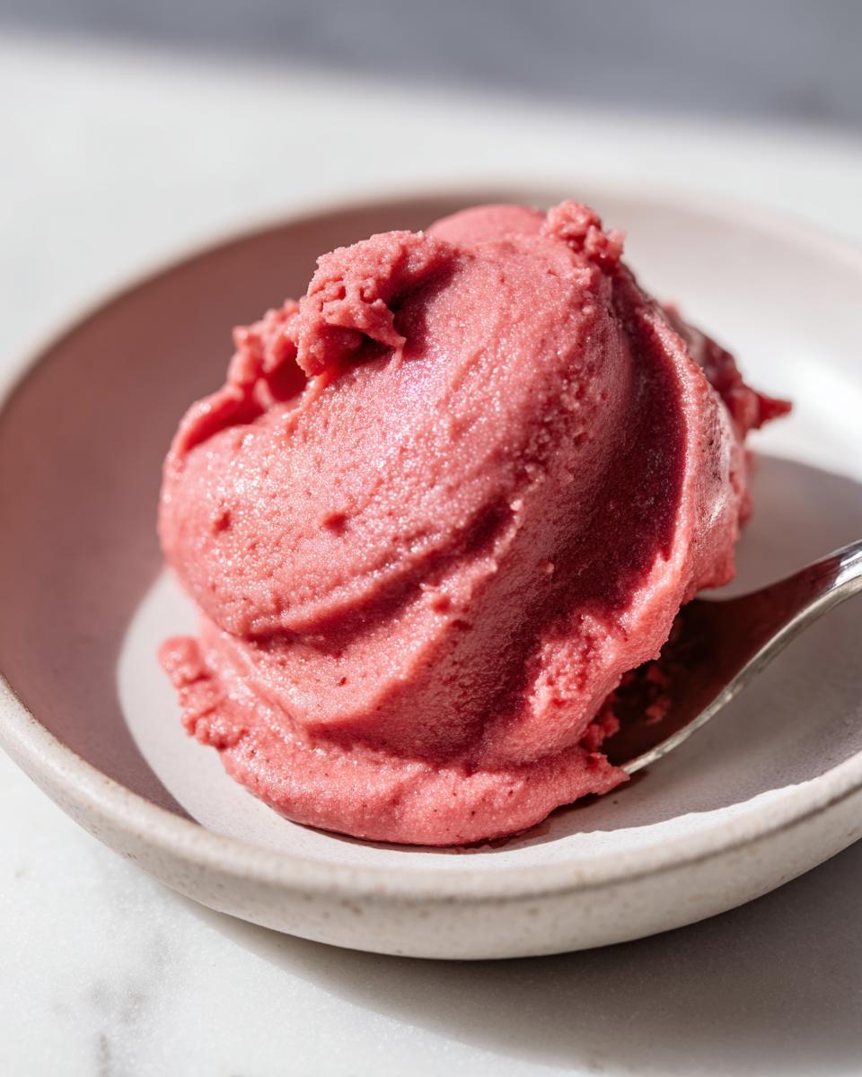 A close-up of a scoop of vibrant pink Cinnamon Rhubarb Butter mixture, served in a small bowl with a spoon.