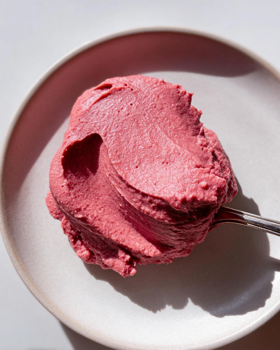 A close-up, overhead shot of a dollop of vibrant pink Cinnamon Rhubarb Butter being scooped onto a light-colored plate.