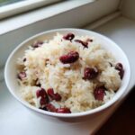 A white bowl filled with fluffy white rice mixed with dark red kidney beans, representing creamy caribbean rice and beans.