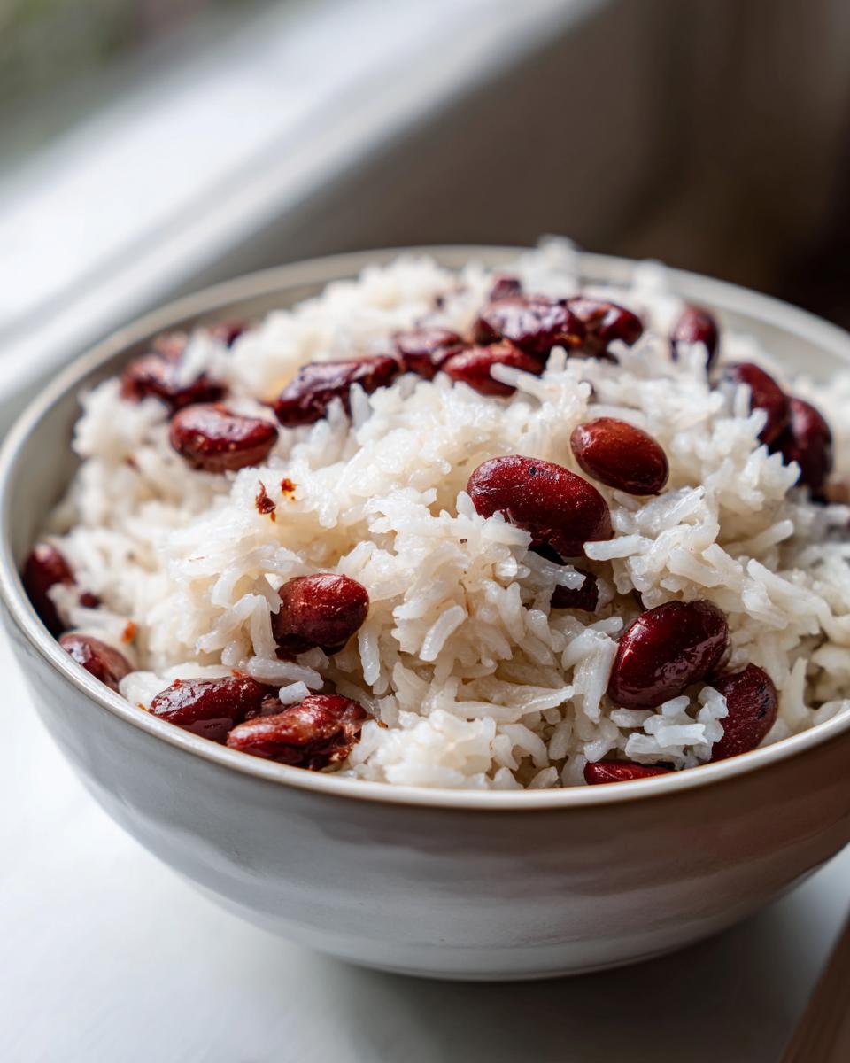 Close-up of fluffy white rice mixed with dark red kidney beans in a light grey bowl, showcasing creamy caribbean rice and beans.