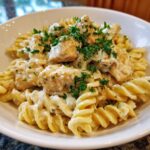 Close-up of fusilli pasta tossed in a creamy garlic parmesan sauce with chunks of chicken and fresh parsley.