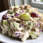 A close-up, appetizing view of creamy chicken salad mixed with celery, red onion, and whole green and red grapes.