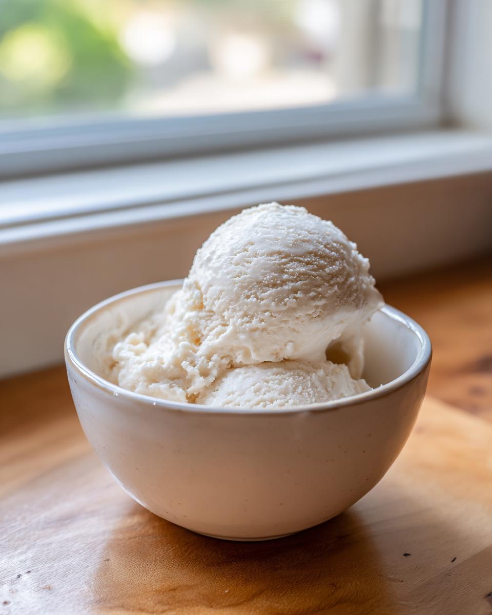 Two scoops of creamy white cottage cheese ice cream served in a small white bowl on a wooden surface.