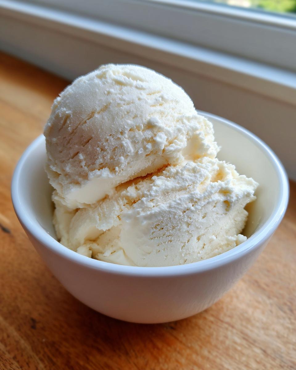 Two scoops of creamy, white cottage cheese ice cream served in a small white bowl on a wooden surface.