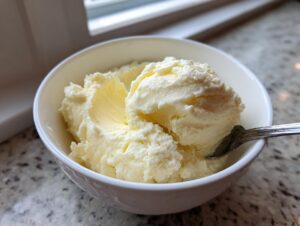 Close-up of creamy, pale yellow homemade vanilla pudding scooped into a white bowl with a spoon.