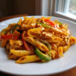 A close-up, appetizing shot of creamy jerk chicken rasta pasta featuring penne, chicken pieces, and colorful bell peppers.