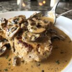 A spoonful of creamy mushroom sauce with sliced mushrooms is lifted off a piece of seared meat.