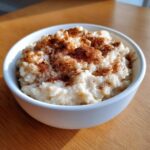 A close-up of a white bowl filled with creamy rice pudding recipe, generously dusted with cinnamon.