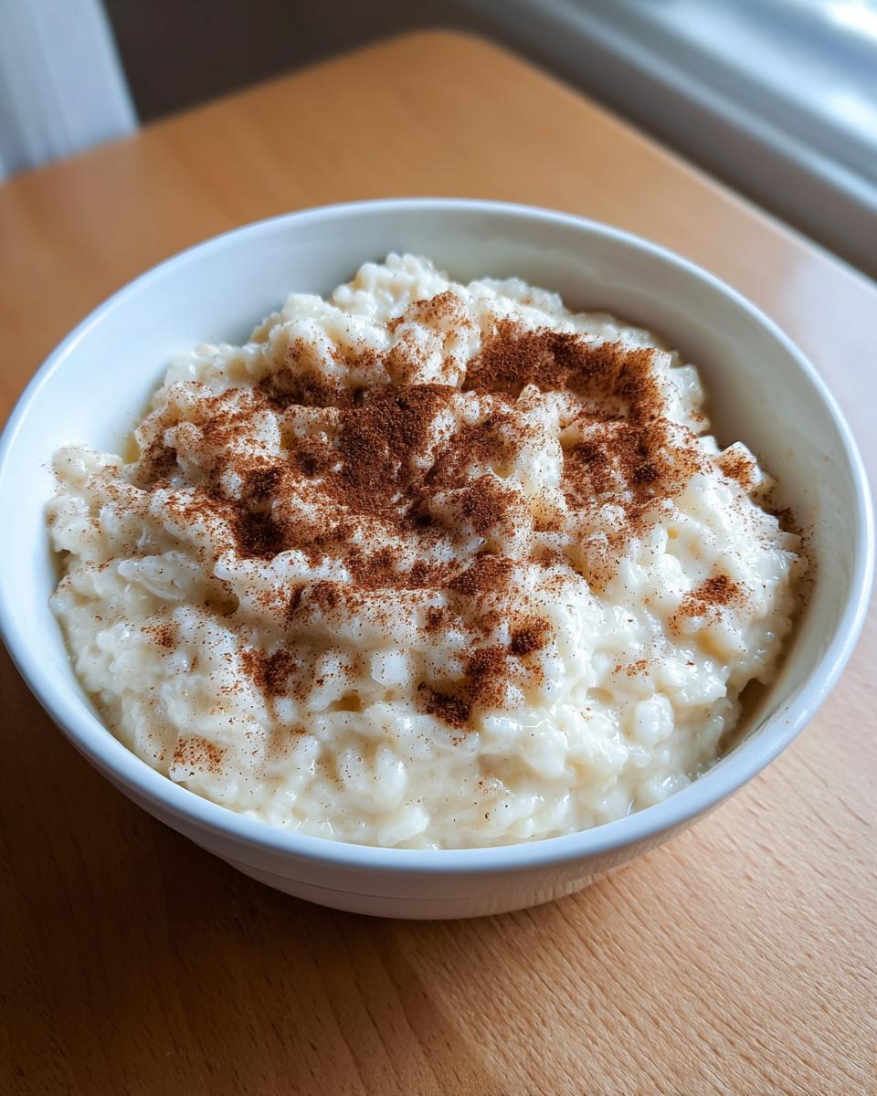 A close-up of a white bowl filled with creamy rice pudding recipe, generously dusted with cinnamon.