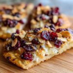Close-up of a slice of crispy flatbread with brie, dried cranberries, and toasted almonds.