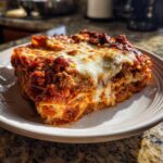 A thick, cheesy slice of crockpot ravioli lasagna with rich meat sauce sitting on a white plate.