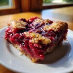 Close-up of a square slice of juicy easy cherry cobbler with a golden crumb topping on a white plate.