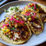 Three grilled Fish Tacos with Rhubarb Pineapple Salsa, featuring blackened fish and pickled red onions on a plate.