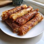 Close-up of several golden brown, lacy crispy rice paper rolls stacked on a white plate.