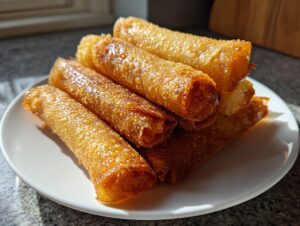 A stack of perfectly golden brown, crispy rice paper rolls glistening under sunlight on a white plate.